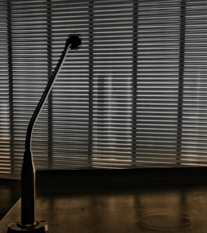 A vertical shot of a lamp on an office table and windows with blinds in the background