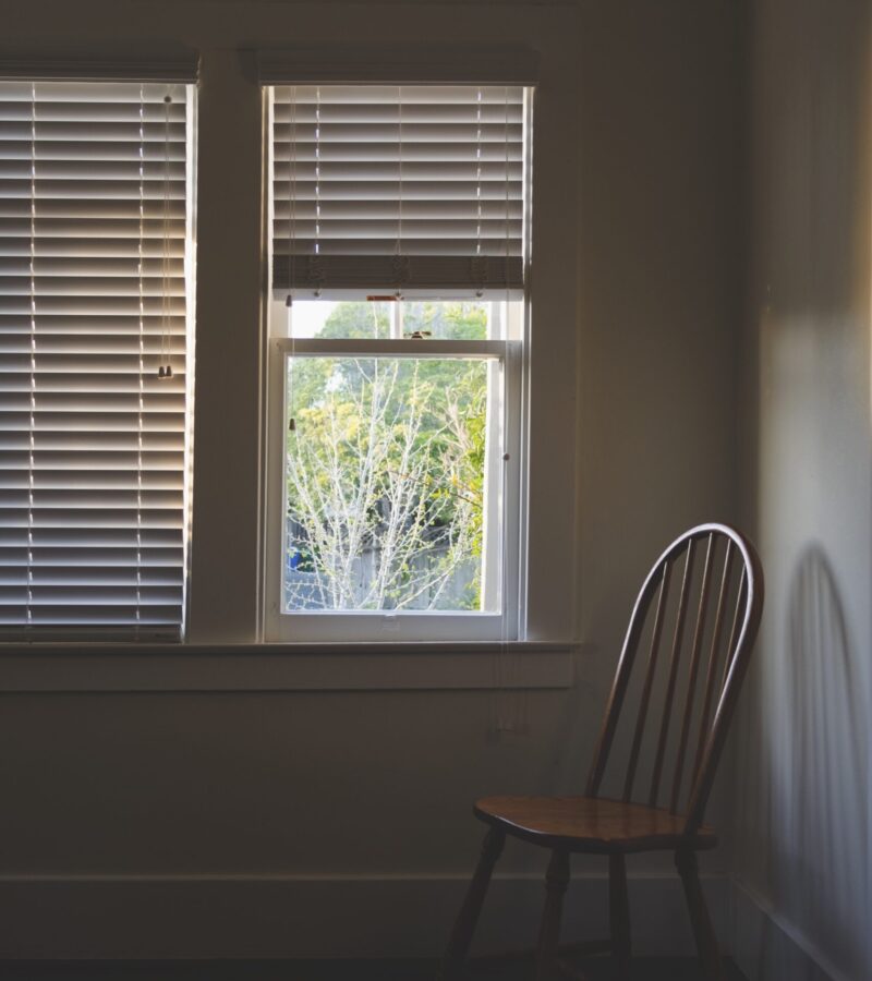 A vertical interior shot of a wooden chair near the window with blinders